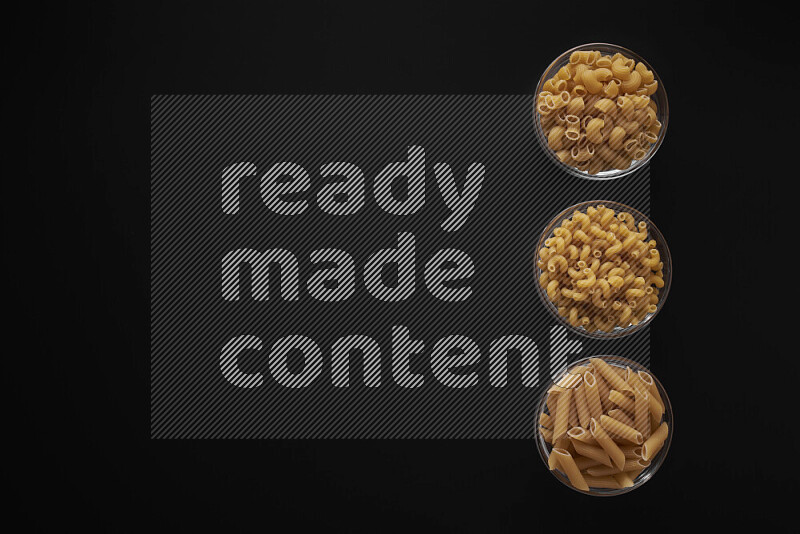 Different pasta types in 3 glass bowls on black background