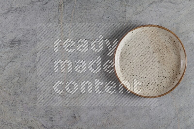 A circular beige pottery plate on grey marble background