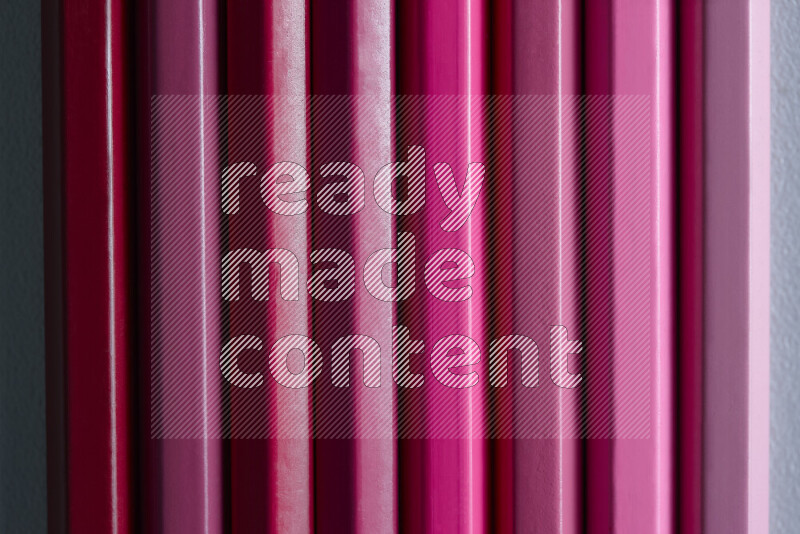 مجموعة من أقلام الرصاص الملونة مرتبة لتعرض تدرجا من الألوان الوردية علي خلفية رمادية