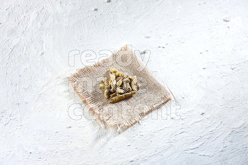 Dried turmeric whole fingers on a piece of burlap on a textured while flooring