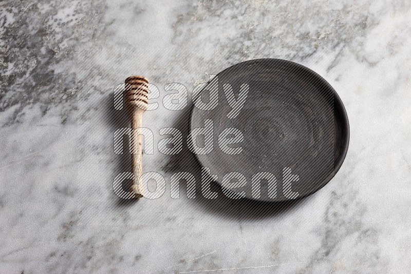 Black Pottery Plate with wooden honey handle on the side with grey marble flooring, 65 degree angle