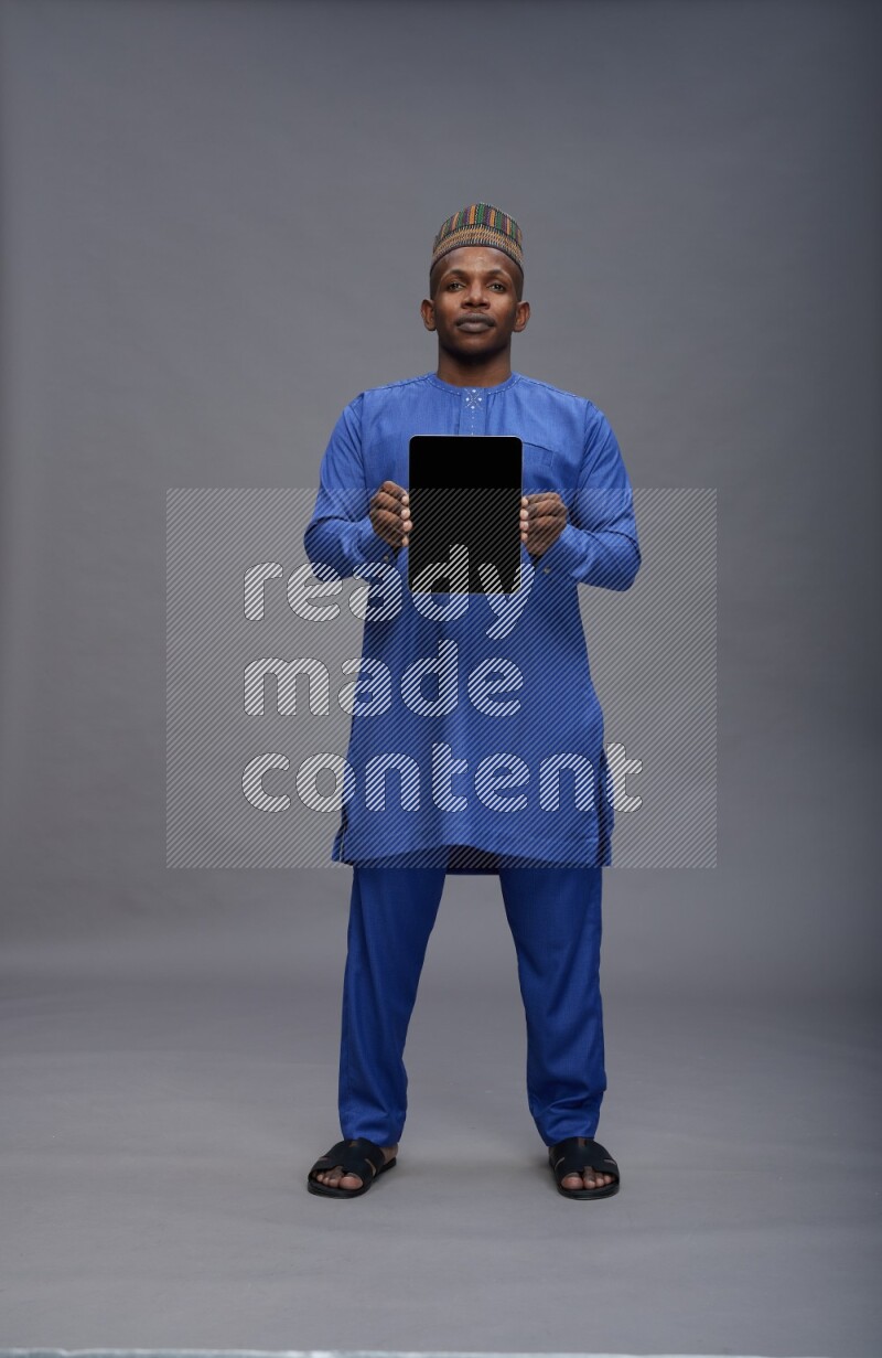 Man wearing Nigerian outfit standing showing tablet to camera on gray background