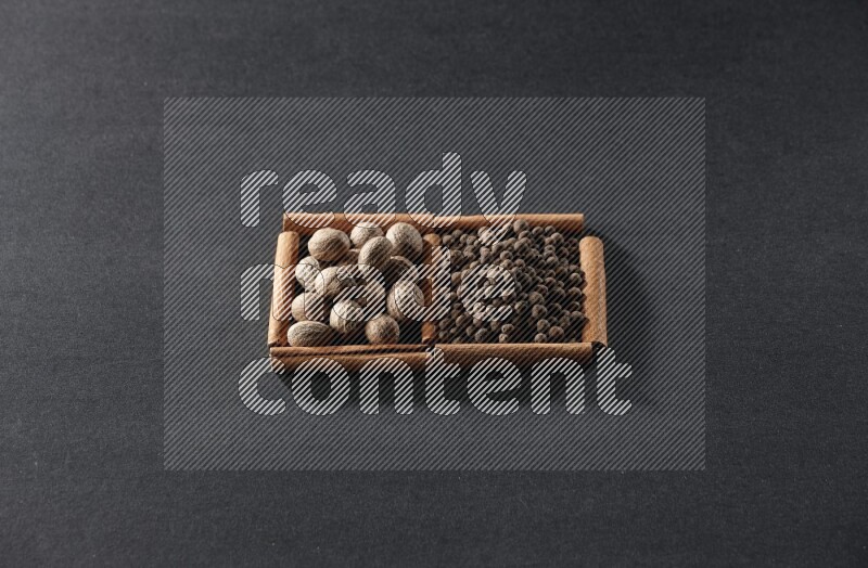 مربعان من أعواد القرفة ممتلئان بجوزة الطيب وحبوب الفلفل الحلو علي خلفية سوداء