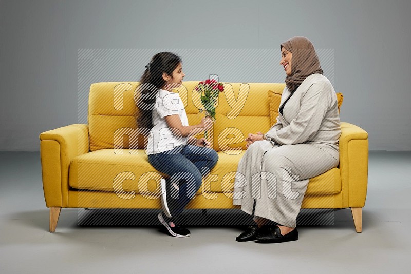 A girl sitting giving flowers to her mother on gray background