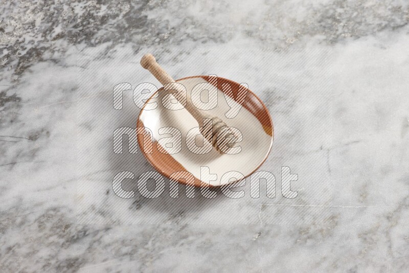 Multicolored pottery plate with wooden honey dipper in it on grey marble background