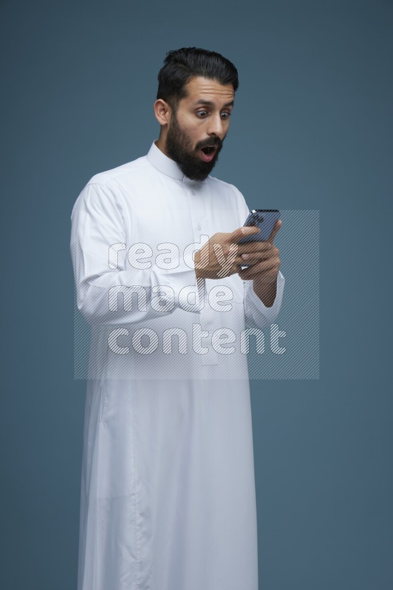 A man Texting in a blue background wearing Saudi Thob