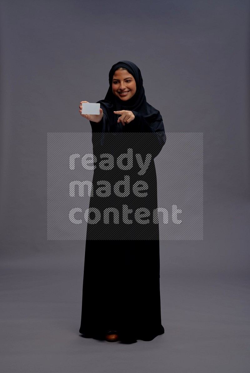 Saudi woman wearing Abaya standing holding ATM card on gray background