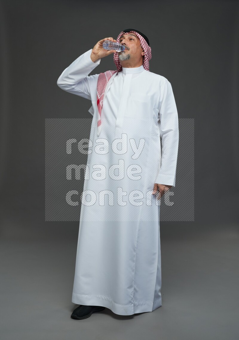 Saudi man with shomag Standing drinking water on gray background