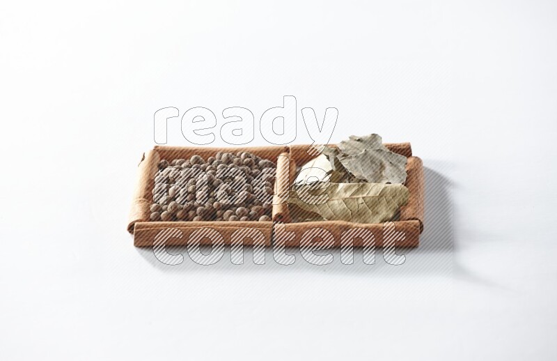 مربعان من أعواد القرفة ممتلئان ببهار الفلفل الحلو وأوراق الغار علي خلفية بيضاء