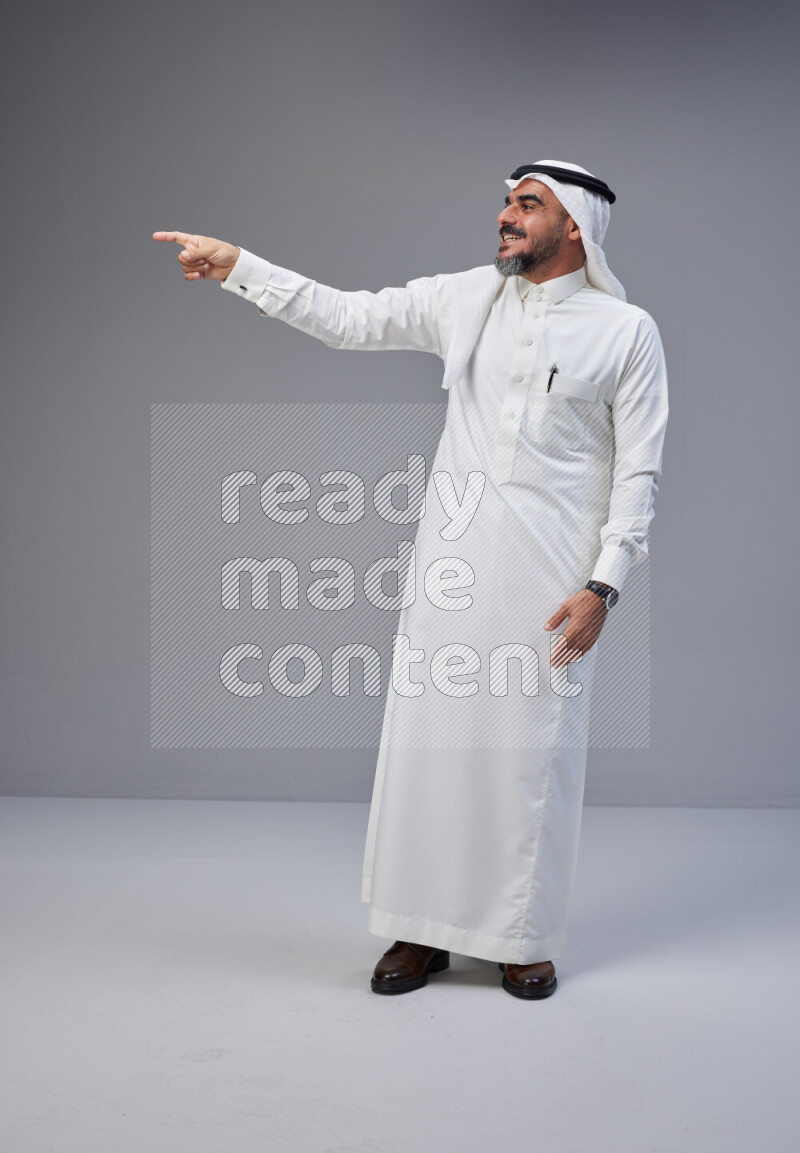 Saudi man Wearing Thob and white Shomag standing interacting with the camera on Gray background