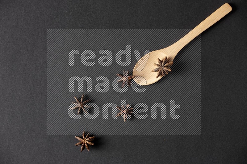 Star Anise in a wooden spoon on more stars anise filling the frame on black flooring
