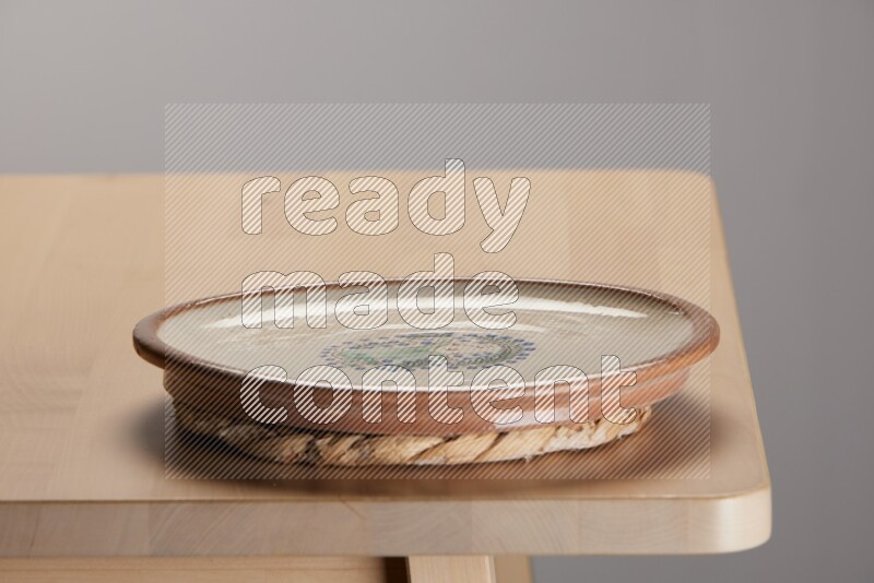 multi-colored pottery Plate placed on a small light colored straw placemat on the edge of wooden table