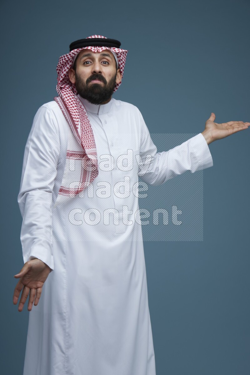 A man pointing in a blue background wearing Saudi Thob and Shomag