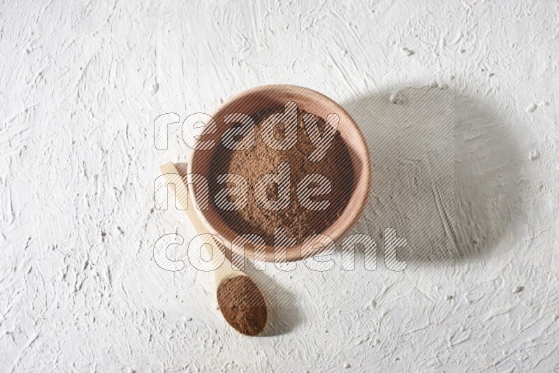 A wooden bowl and a wooden spoon full of cloves powder on a textured white flooring