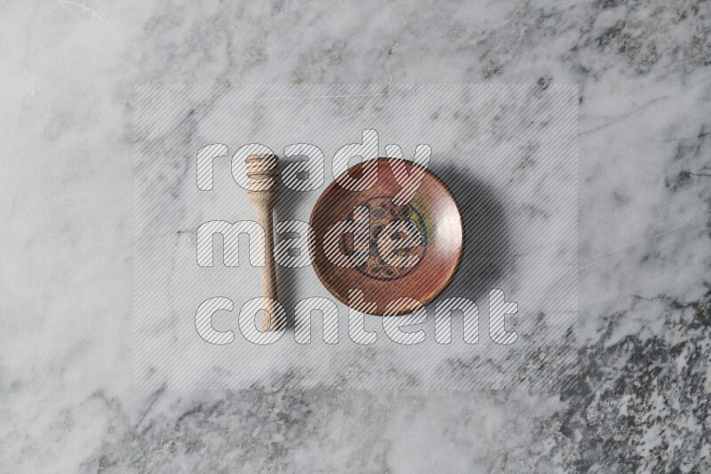 Decorative pottery plate with wooden honey dipper on the side on grey marble background