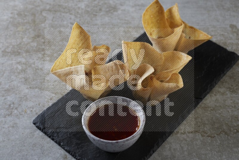 wonton cups with soy sauce ramkin on rectangle slate on grey textured counter top