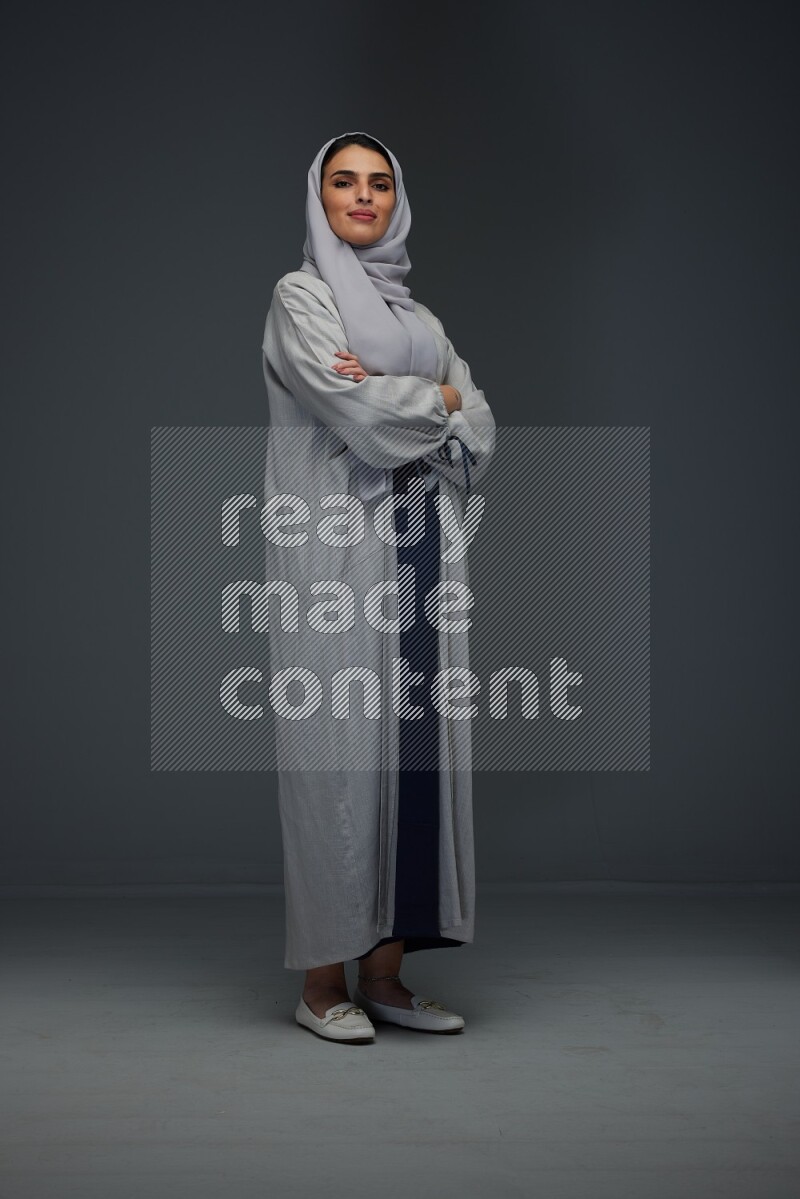 A Saudi woman wearing a light gray Abaya and head scarf standing and making multi poses eye level on a grey background