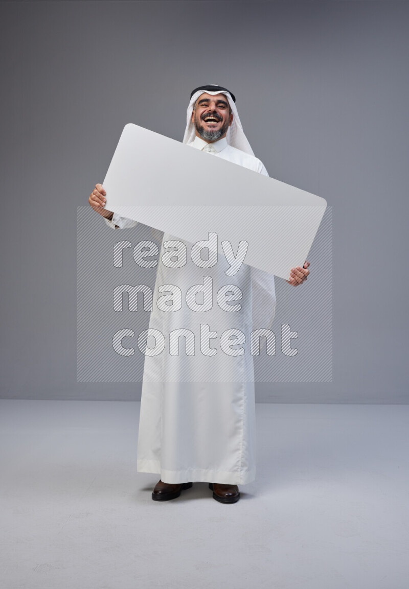 Saudi man Wearing Thob and white Shomag standing holding board on Gray background