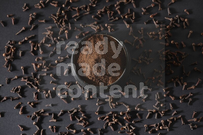 وعاء فخاري أسود ممتلئ ببودرة القرنفل وحبوب القرنفل على خلفية سوداء