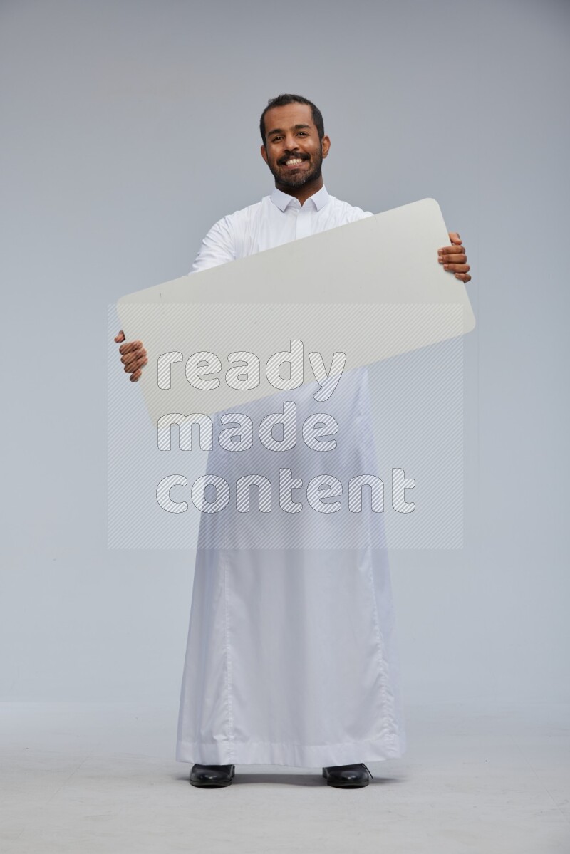 Saudi man wearing Thob standing holding board on Gray background