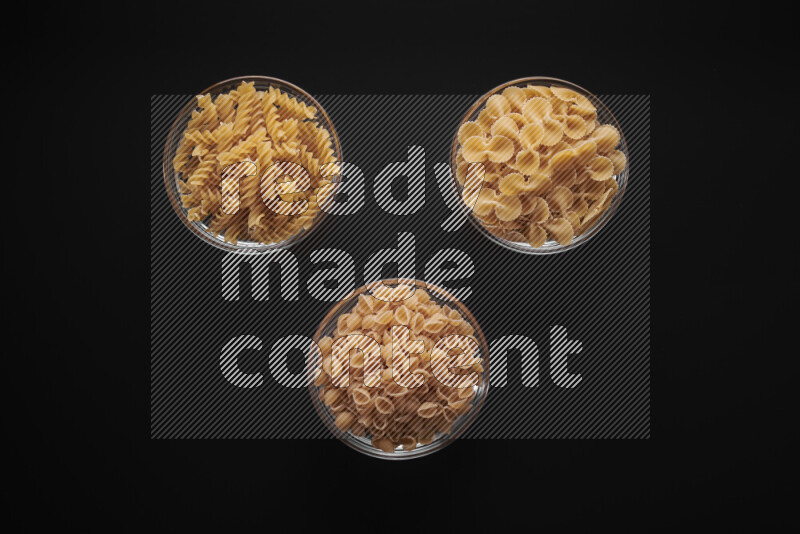Different pasta types in glass bowls on black background