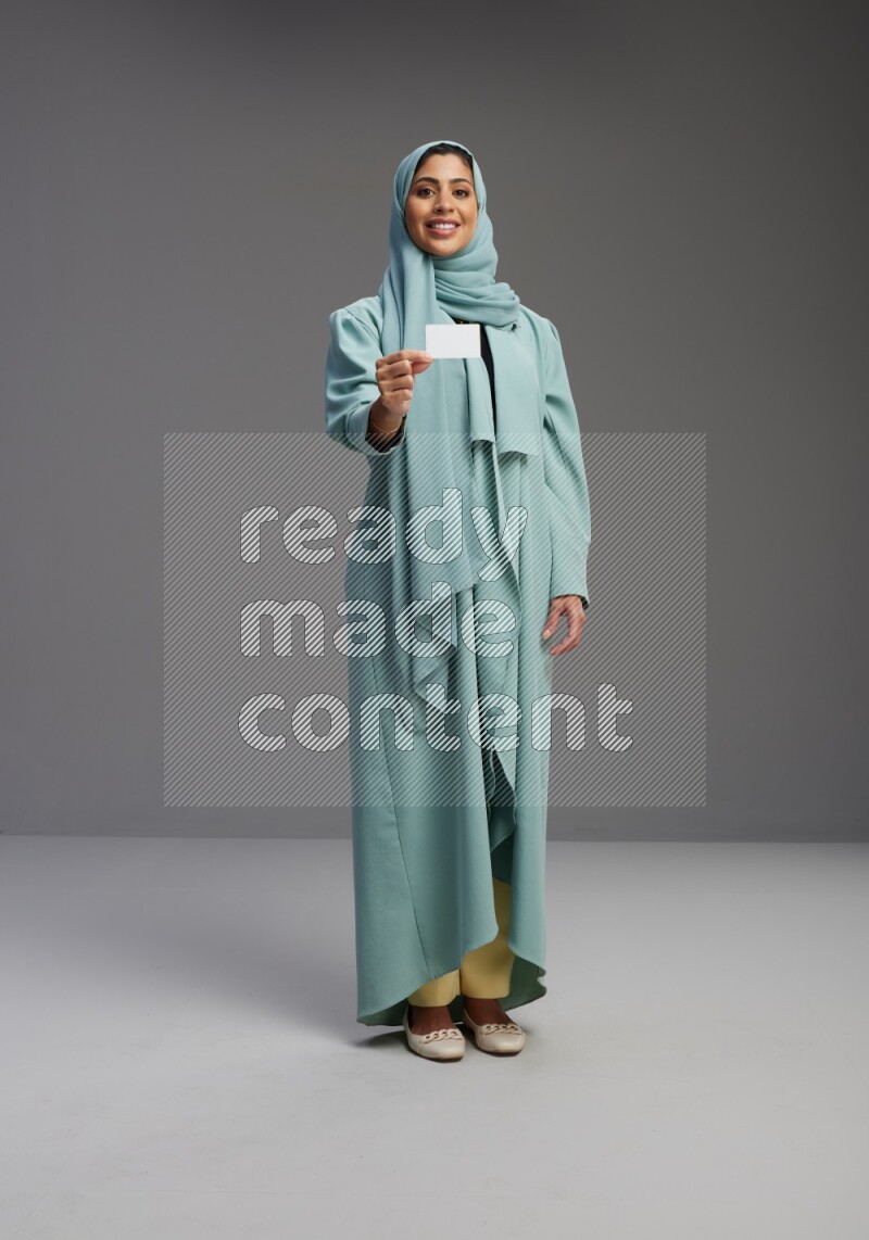 Saudi Woman wearing Abaya standing holding ATM card on Gray background