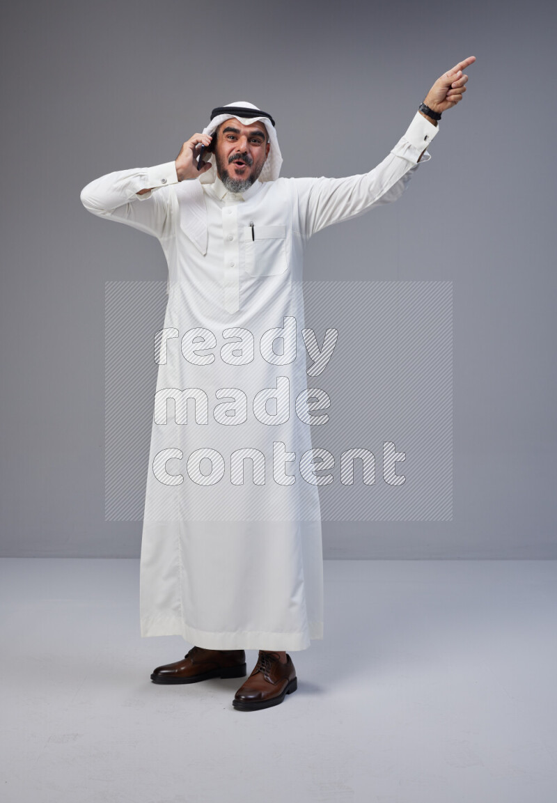 Saudi man Wearing Thob and white Shomag standing talking on phone on Gray background
