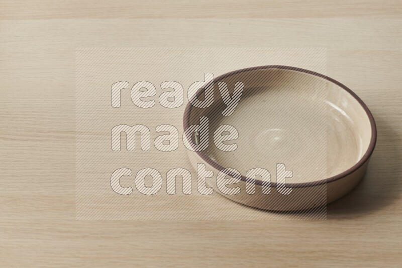 A beige pottery oven bowl on light wooden background