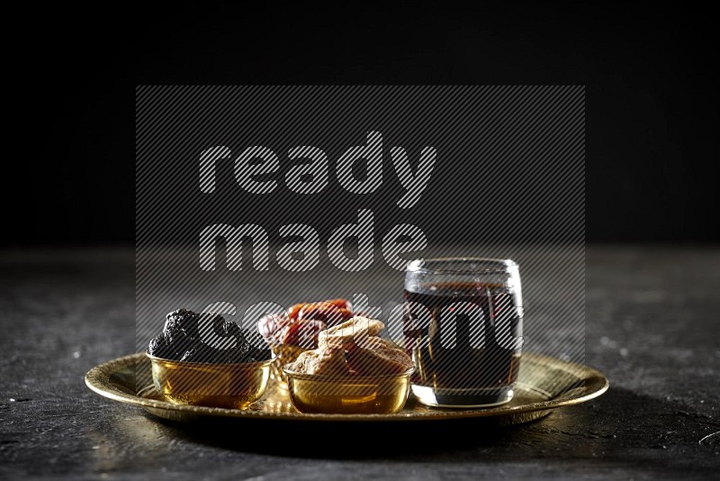 Dried fruits in metal bowls with tamarind on a tray in dark setup