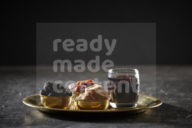 Dried fruits in metal bowls with tamarind on a tray in dark setup