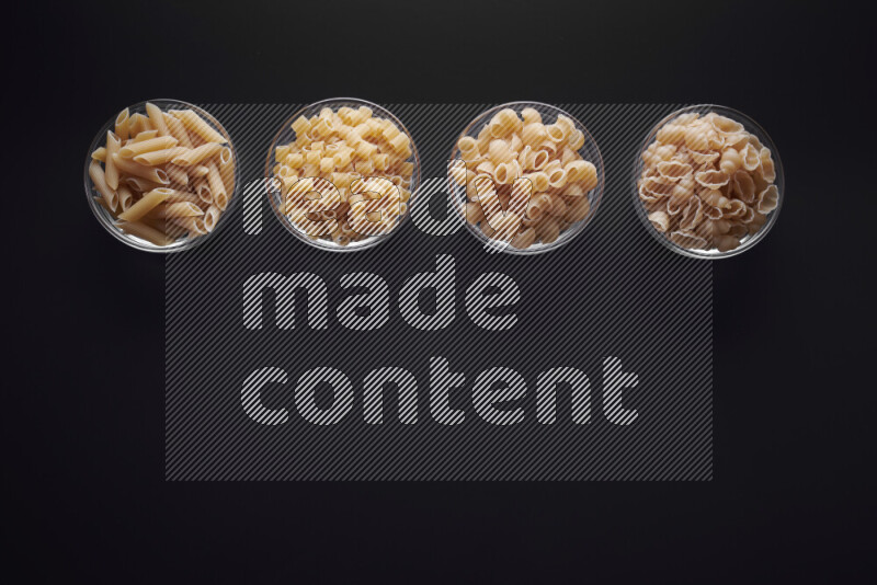 Different pasta types in glass bowls on black background