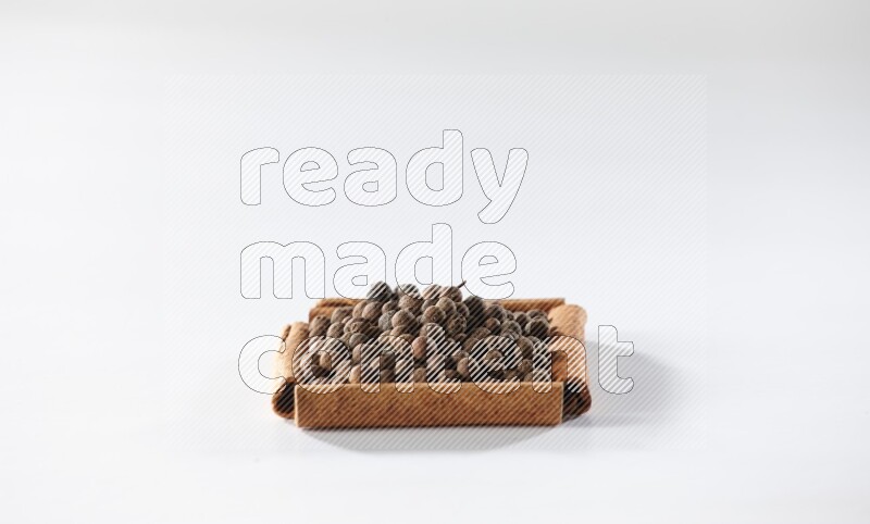 أربعة من أعواد القرفة مكونة شكل مربع بداخلها بهار الفلفل الحلو علي خلفية بيضاء