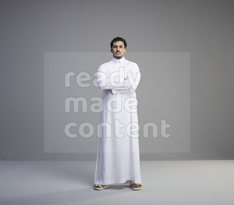 A Saudi man standing wearing thob with face painting interacting with the camera on gray background