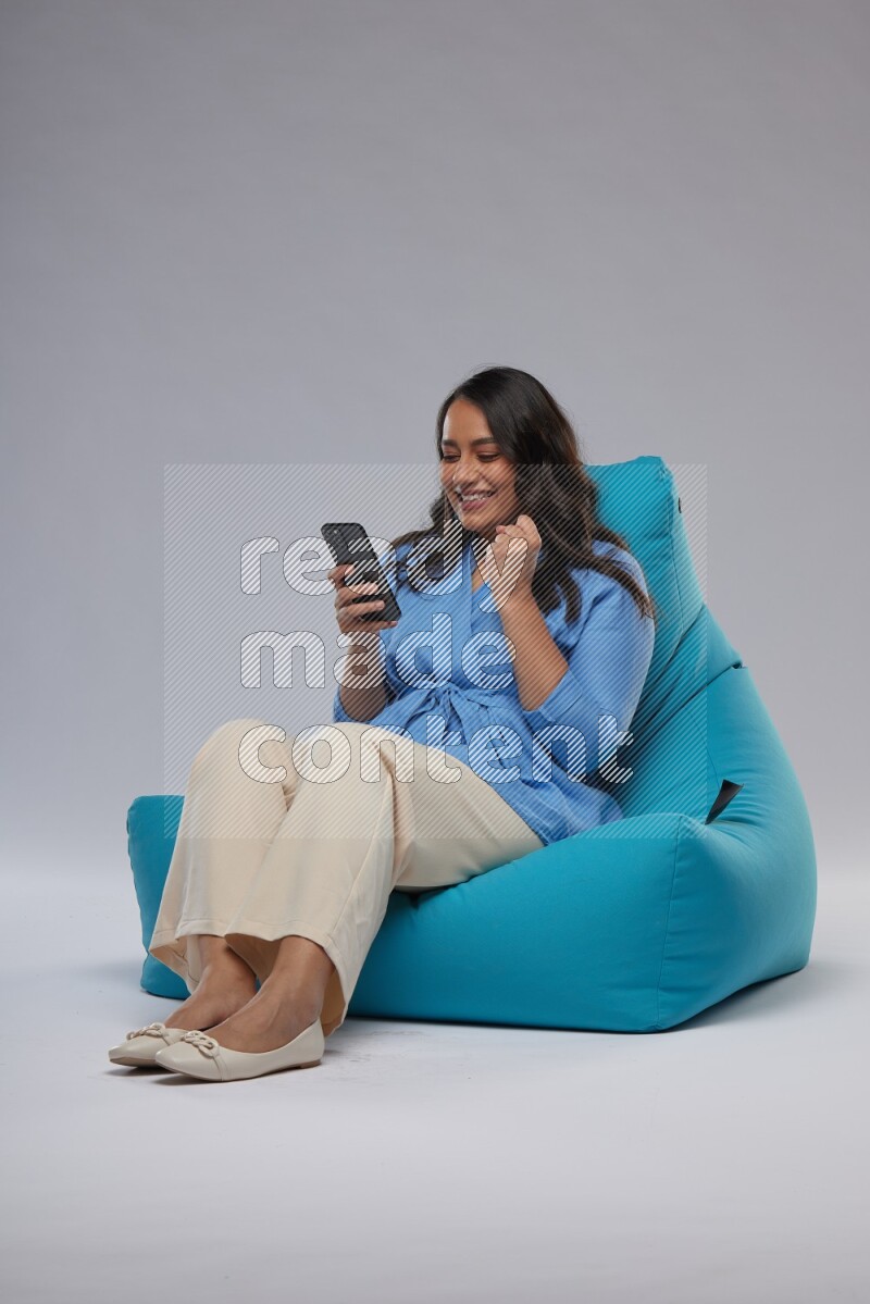 A woman sitting on a blue beanbag and texting on phone
