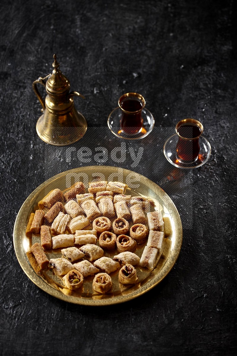 حلويات شرقية مع الشاي وإبريق معدني علي خلفية سوداء خشبية