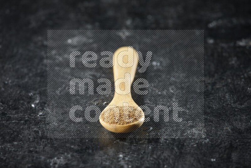 ملعقة خشبية ممتلئة ببودرة الكمون على خلفية سوداء