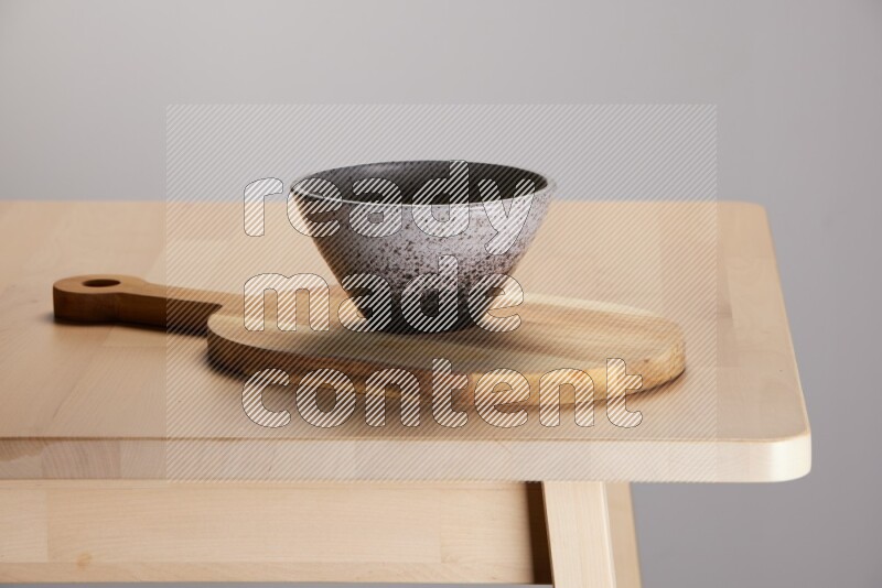 multi colored bowl placed on a  wooden oval cutting board on the edge of wooden table