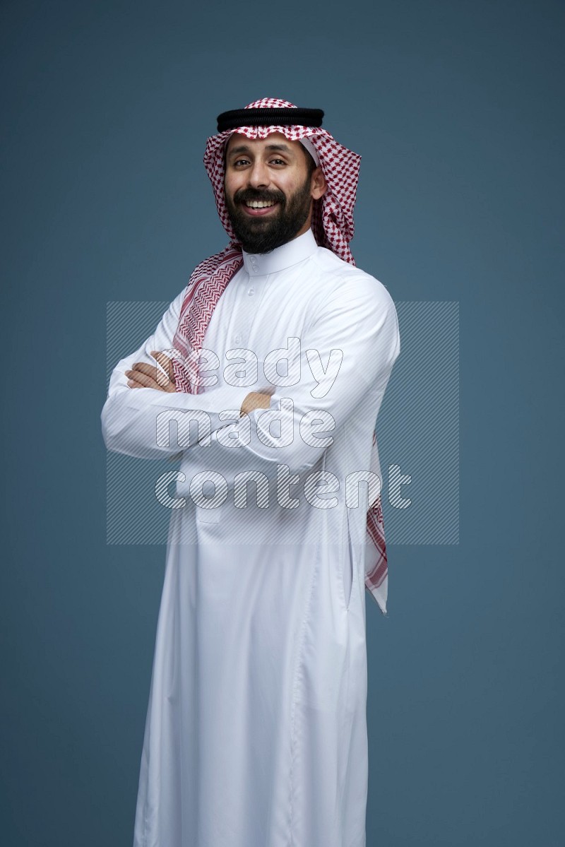 A man posing in a blue background wearing Saudi Thob and Shomag