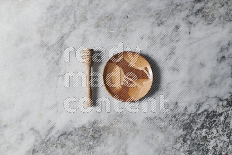 Multicolored Pottery Plate with wooden honey handle on the side on grey marble flooring, Top view