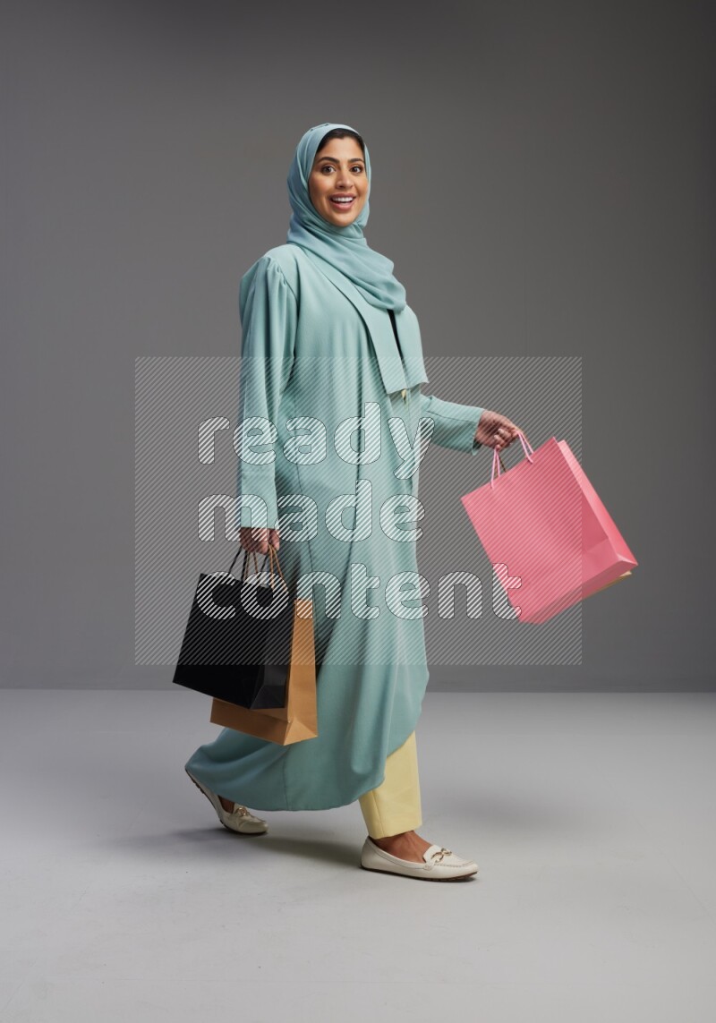 Saudi Woman wearing Abaya standing holding shopping bag on Gray background