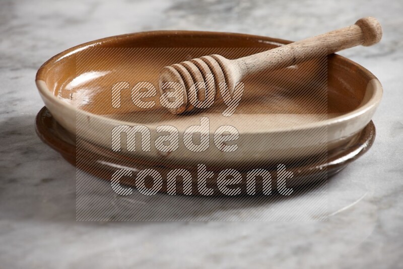 Multicolored pottery oven plate with wooden honey handle in it on grey marble background