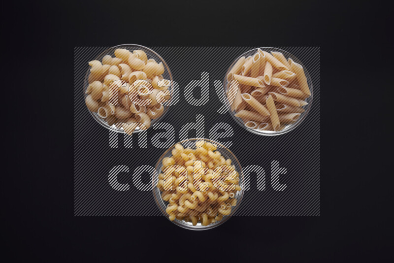 Different pasta types in glass bowls on black background