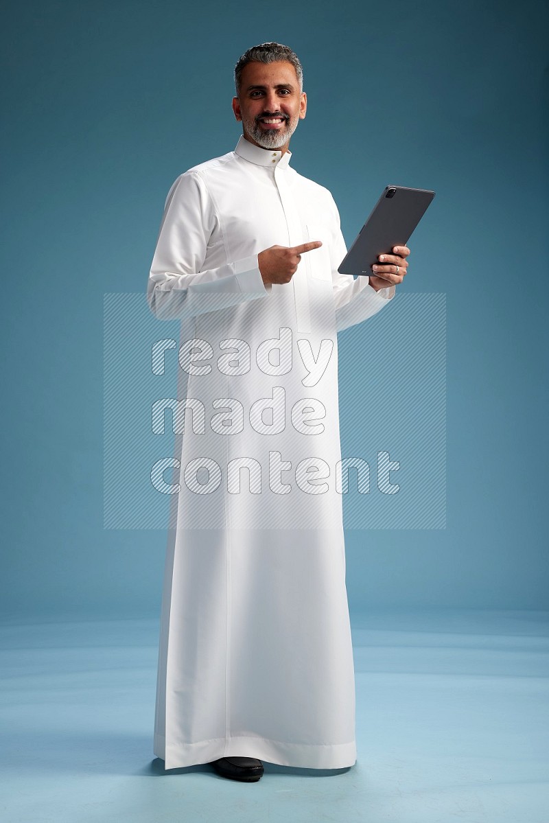 Saudi man waring thob with tablet on blue background