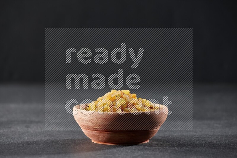 وعاء خشبي ممتلئ بالزبيب الأصفر على خلفية سوداء