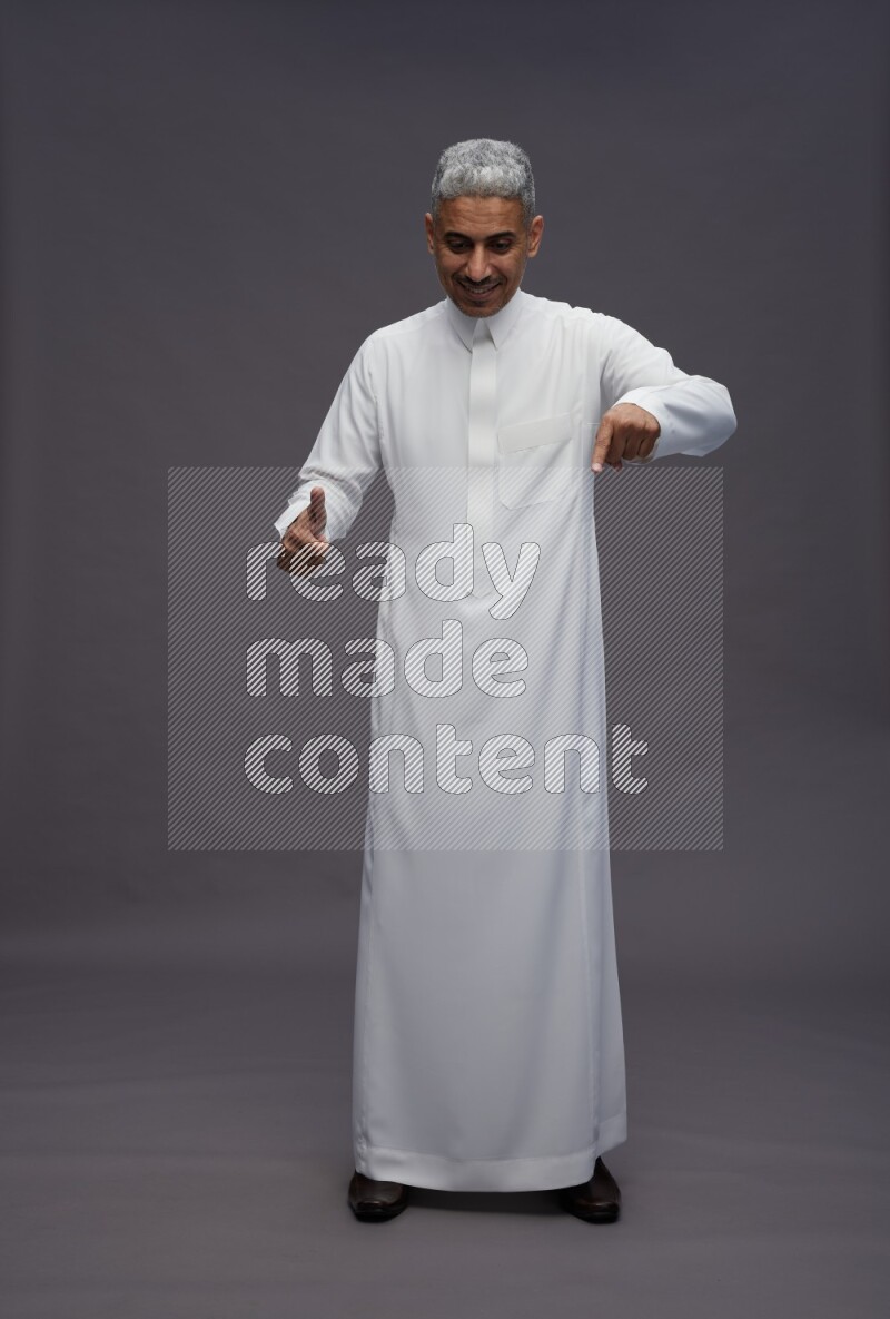 Saudi man wearing thob standing interacting with the camera on gray background