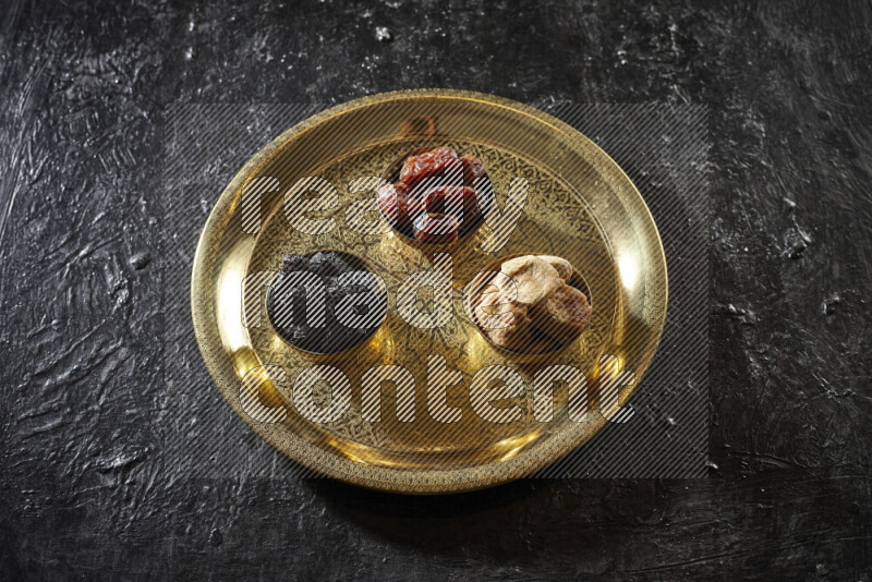 Dried fruits in metal bowls on a tray in a dark setup