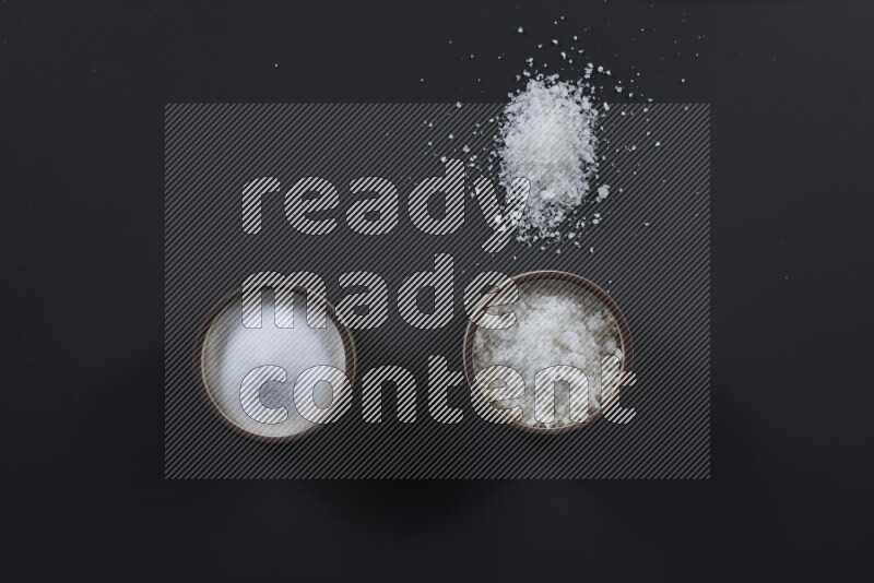 وعاء فخاري ممتلئ بملح الطعام الناعم وملح البحر الخشن على خلفية سوداء