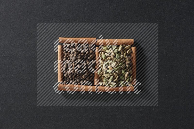 مربعان من أعواد القرفة ممتلئان ببهار الفلفل الحلو وحب الهيل علي خلفية سوداء