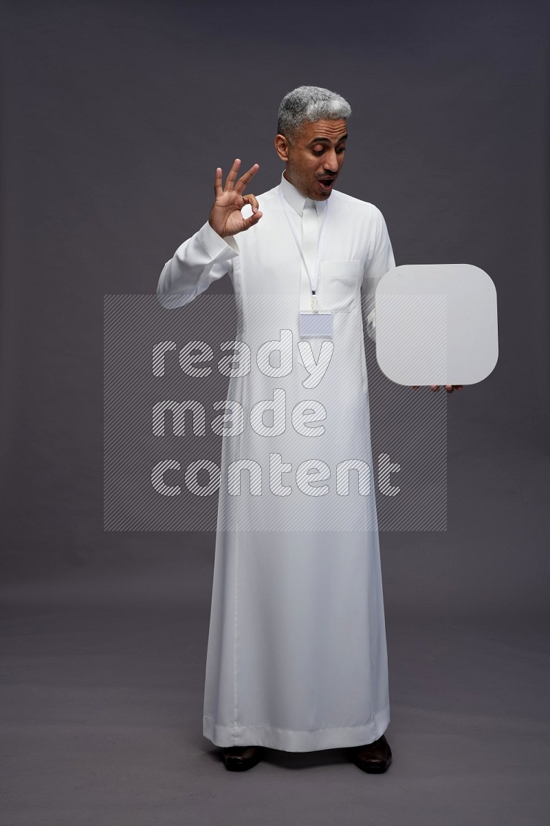 Saudi man wearing thob with neck strap employee badge standing holding social media sign on gray background