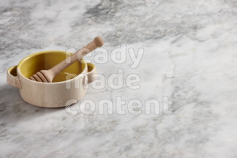 Multicolored pottery bowl with wooden honey dipper in it on grey marble background
